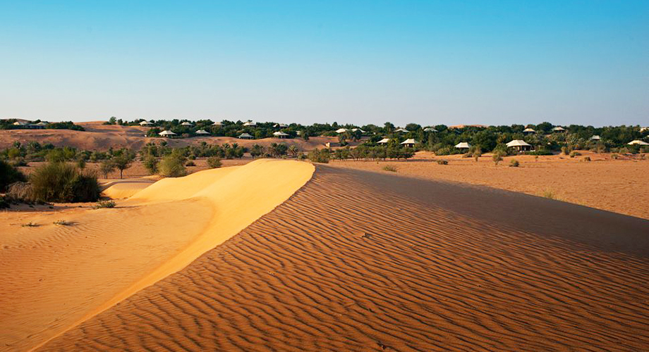 Sand dunes in the Arabian Desert where the Al Maha Resort can be seen at a distance